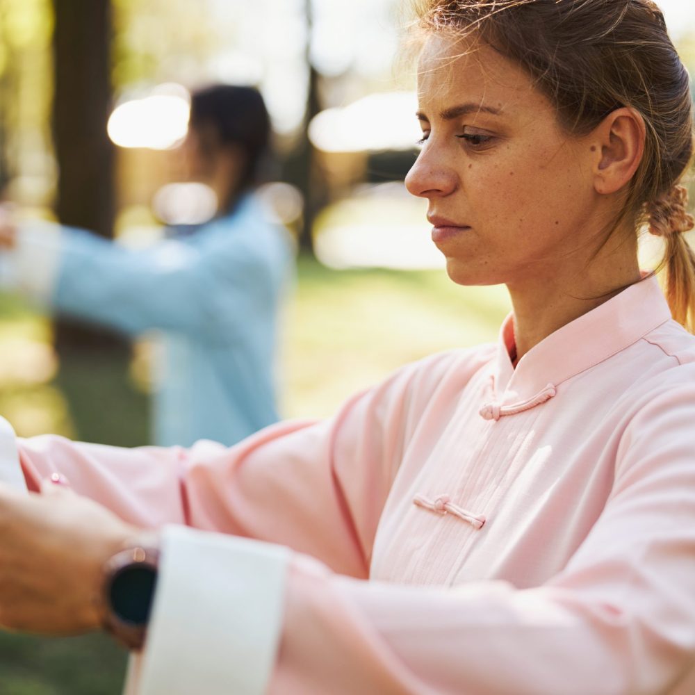 Serious Caucasian woman in pink clothes pulling out her arms in front of her chest during wushu workout